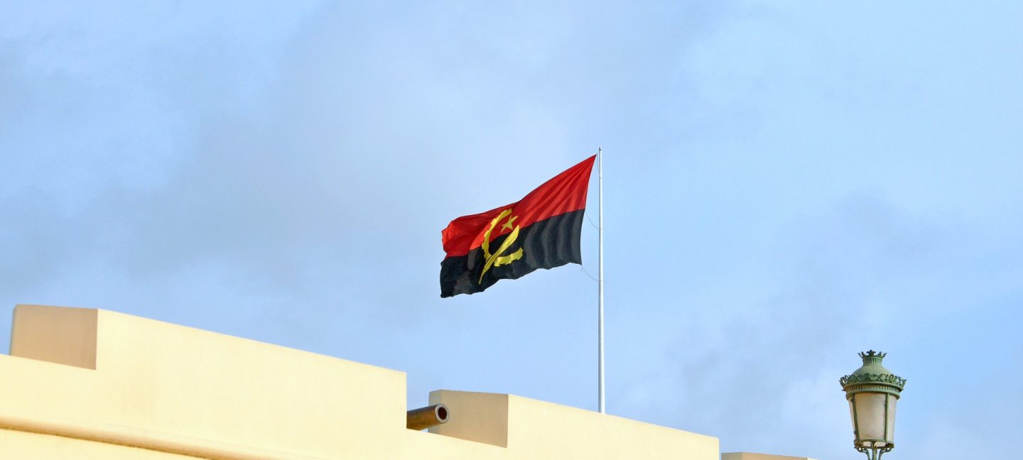 Angolan Flag mounted on top a city wall with blue sky in the background