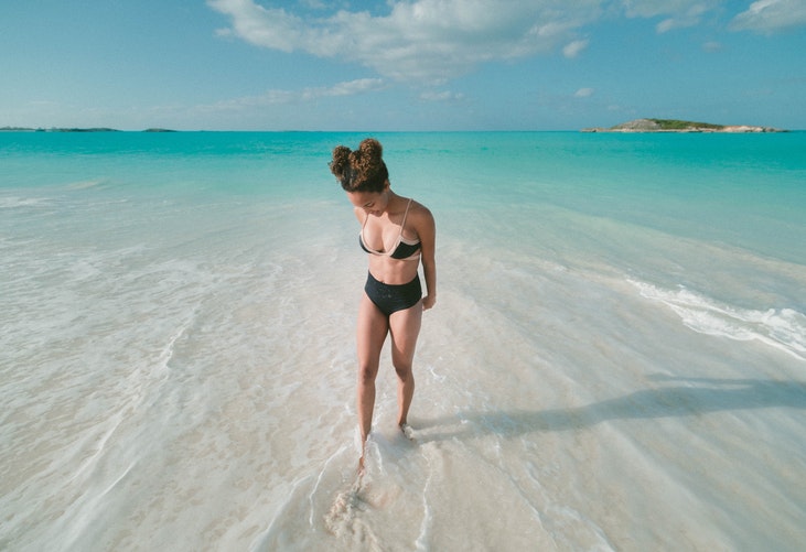Woman standing in water as the tide pulls the turquoise water away with islands in the distance