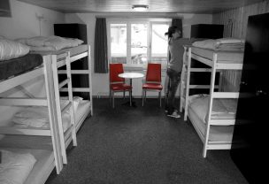 Gray picutre of bunk beds in a hostel room with contrasting red chairs