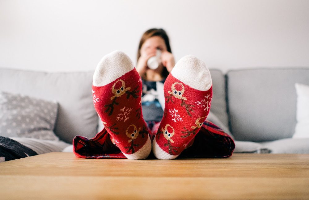 Woman sitting on a couch drinking from a mug and holding her feet in red socks up on the table