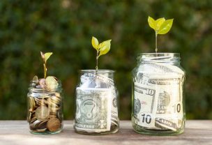 Small plants sprouting out of glass jars filled with paper money and coins