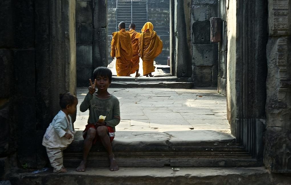Kids sitting on the entrance stairs of the temple and monks in background