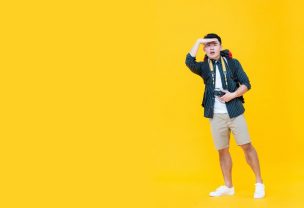 Asian tourist man looking away with hand on forehead isolated on yellow background with copy space