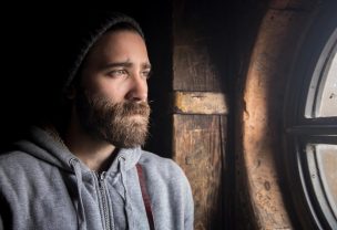 Image of a bearded man in a beanie looking through the window with a longing expression